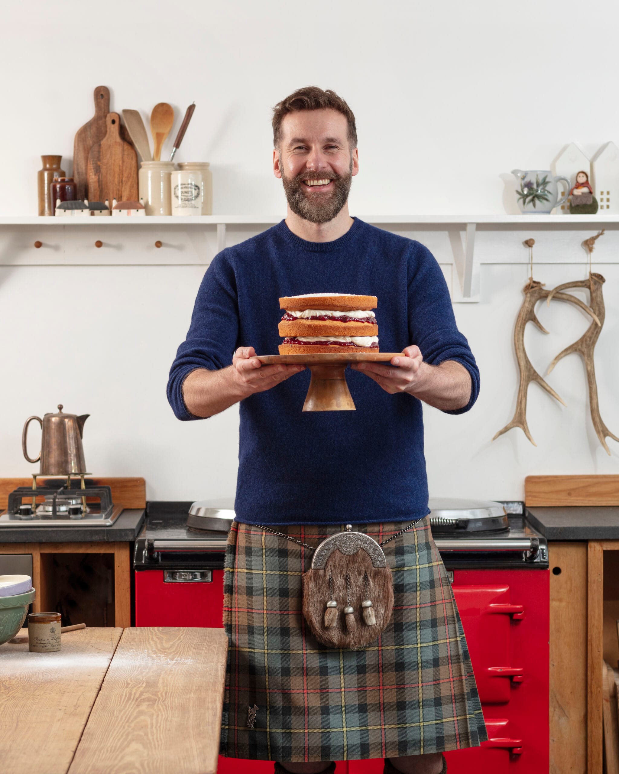 The Hebridean Baker holding a cake in his kitchen